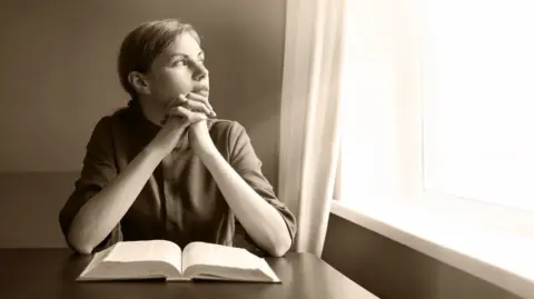 A woman with an open bible longs for wisdom and love, searching for light amidst the darkness